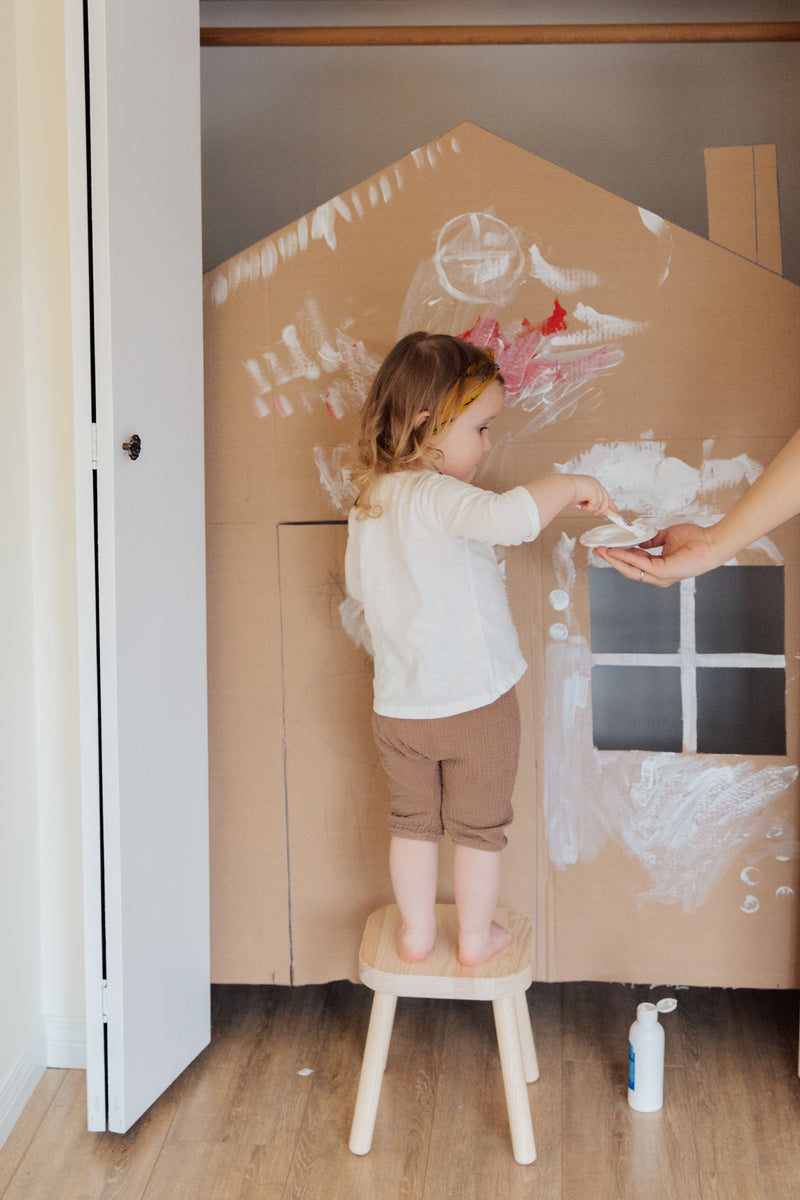 Girl in white shirt painting a cardboard cut-out of a home to symbolise home building 
